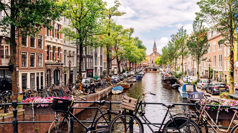 Bicycles parked along Amsterdam's canals with historic gabled canal houses in the background