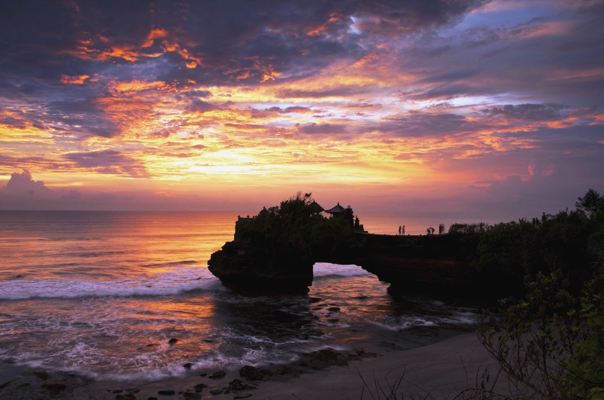 Tanah Lot temple at sunset in Bali &mdash; a sea temple perched on a rocky outcrop