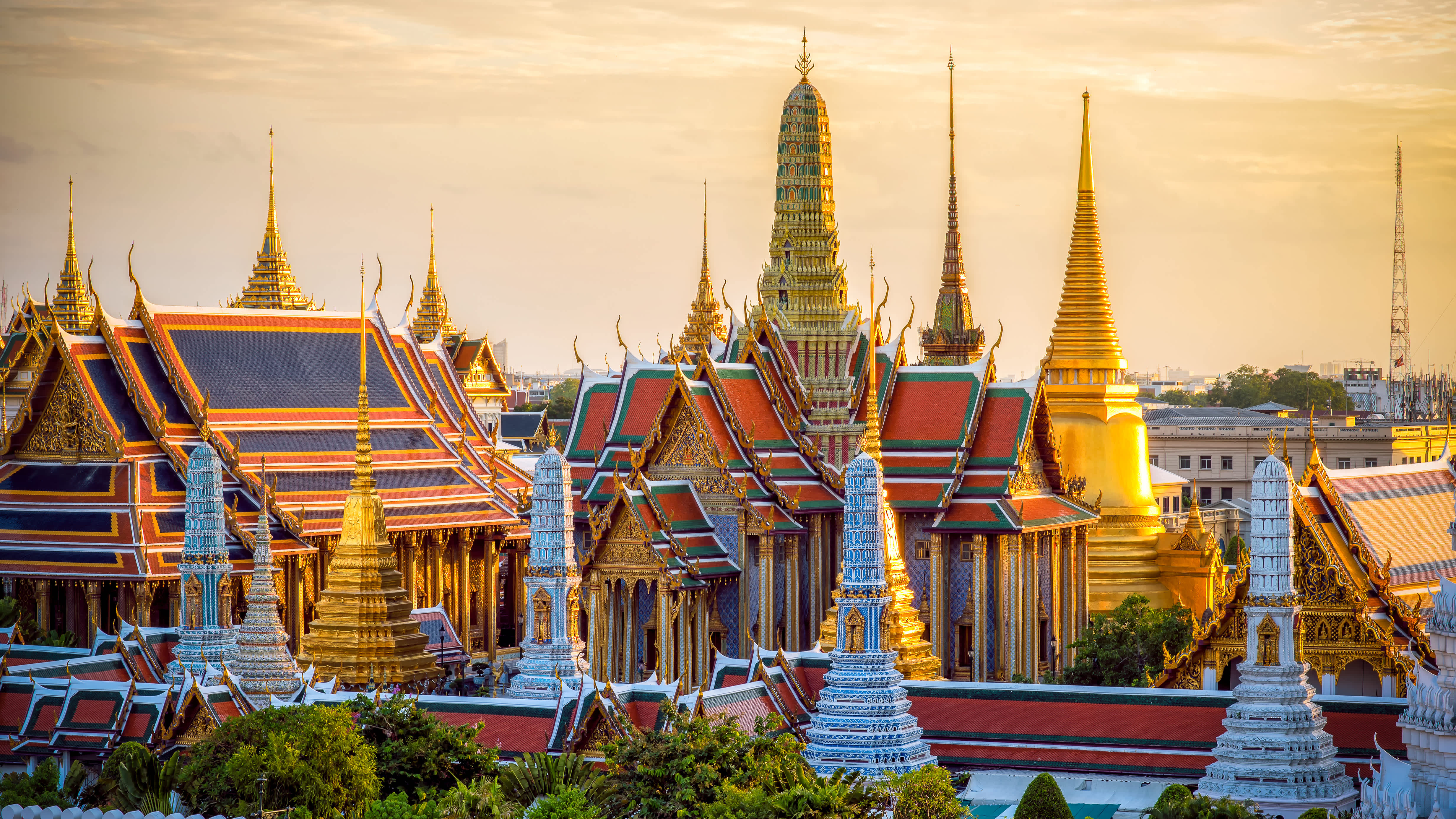 A majestic view of Wat Arun (Temple of Dawn) across the Chao Phraya River, bathed in golden hour light with traditional longtail boats passing by.