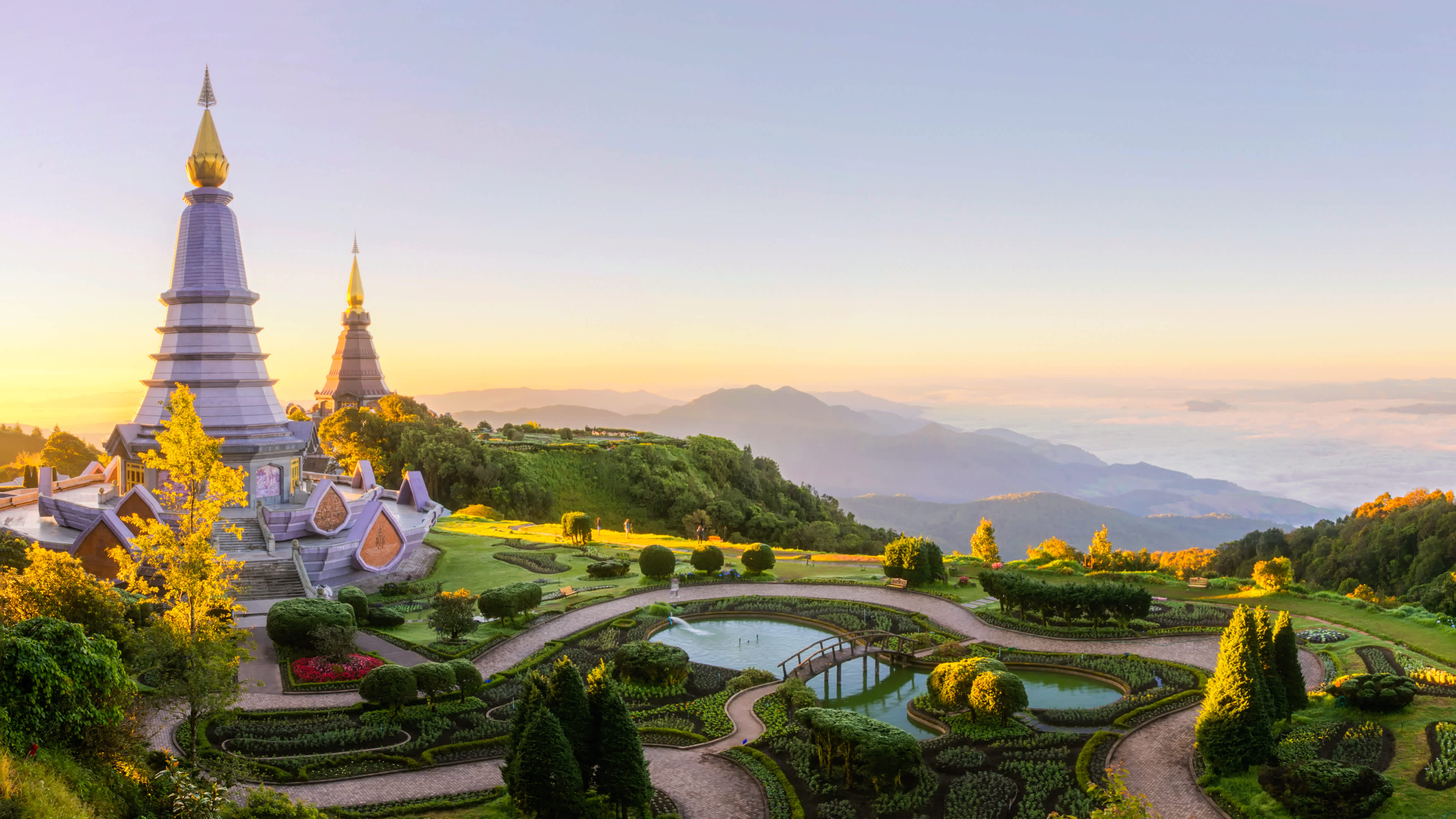 The intricate golden chedi of Wat Phra That Doi Suthep gleams against a lush green mountain backdrop, with a panoramic view of Chiang Mai below.