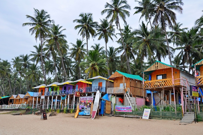 Goa beach shacks and colorful fishing boats on a North Goa beach at sunset — the classic Goan beach experience with colorful umbrellas, cold beer, and the Arabian Sea in the background