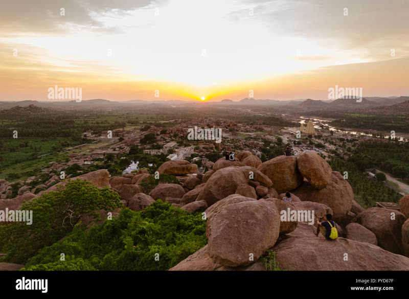 Hampi's boulder landscape at sunset — enormous granite rocks casting long shadows over the Tungabhadra river basin with banana plantations and temple ruins visible in the distance