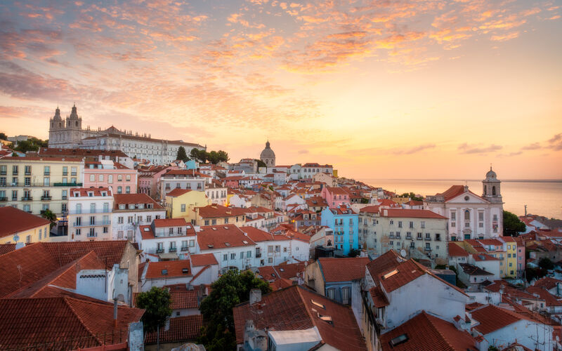 Lisbon's Alfama district at sunrise, colourful tiled buildings and the Tagus River stretching to the horizon