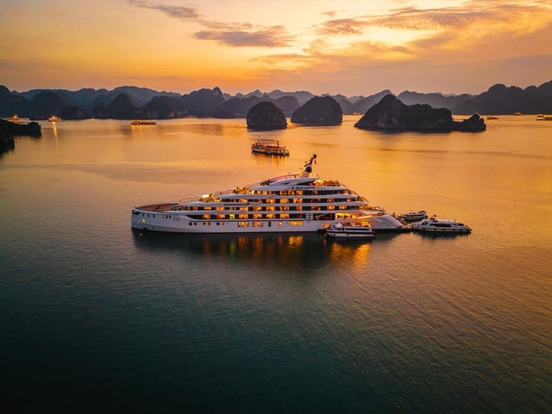 Traditional junk boat cruising among Ha Long Bay's limestone karst islands with other cruise vessels visible in the distance