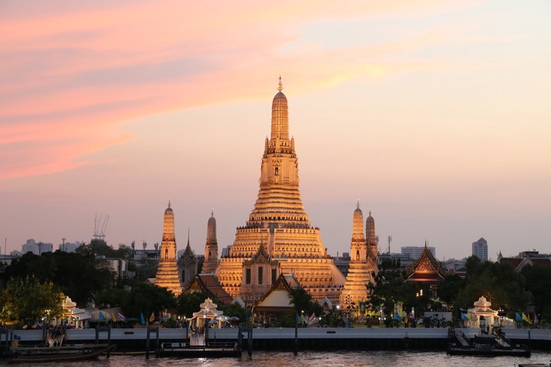 Wat Arun temple at sunset in Bangkok, Thailand — ornate spires reflected in the Chao Phraya river
