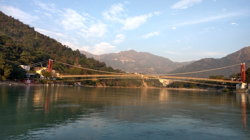 Laxman Jhula suspension bridge over the sacred Ganges River in Rishikesh — the iconic iron footbridge connecting both banks, surrounded by ashrams and ghats in the foothills of the Himalayas