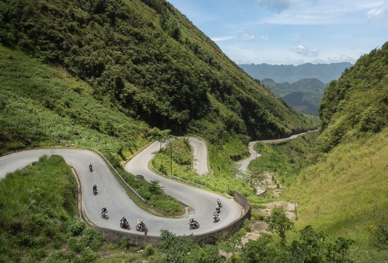 Ha Giang Loop's dramatic mountain road winding through the karst plateau of Dong Van with motorbike travelers