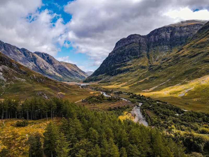 Glencoe Valley in the Scottish Highlands — dramatic glacial valley with towering peaks reflected in the still river below