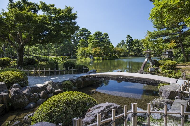 Kenroku-en garden in Kanazawa with stone lantern reflected in a calm pond surrounded by manicured trees
