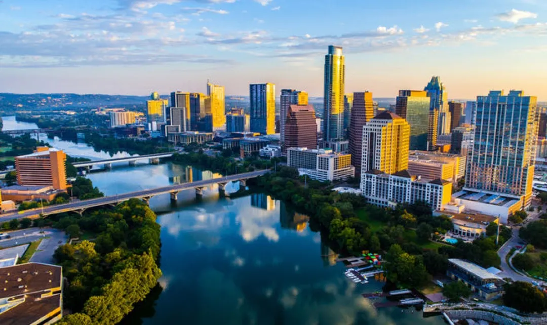 Vibrant scene of people paddleboarding on Lady Bird Lake with the Austin downtown skyline at sunset.
