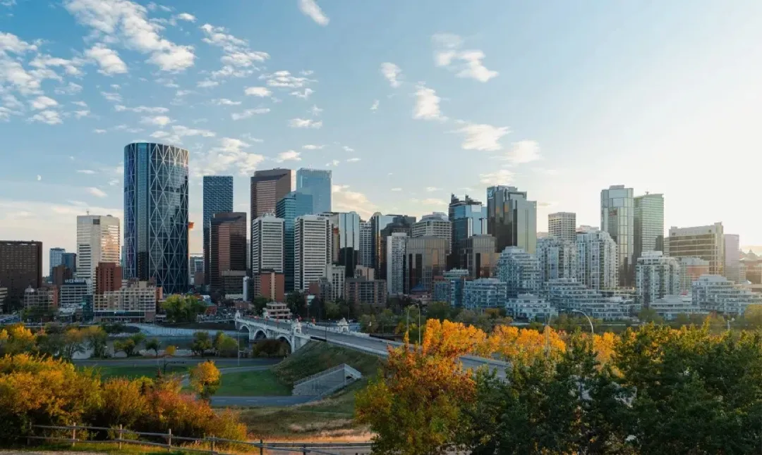 Modern Calgary skyscrapers framed by distant Rocky Mountains under a vast blue sky, with the iconic Calgary Tower prominent.