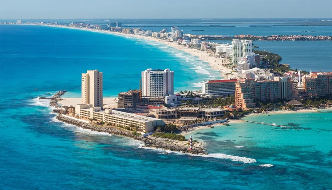 Vast turquoise Caribbean sea meeting the pristine white sands of Playa Delfines in Cancun, with a 'Cancun' sign prominent.