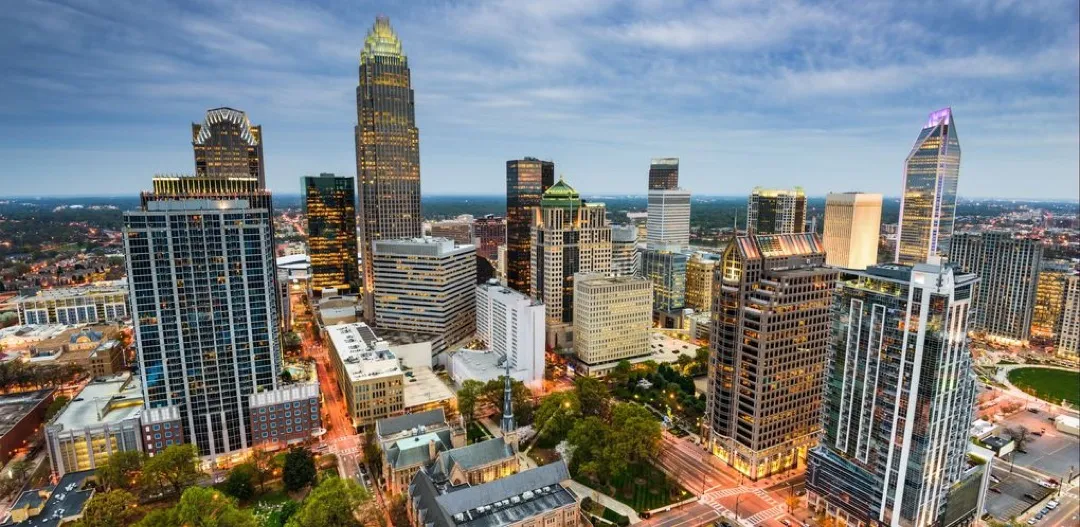 Modern skyscrapers of Uptown Charlotte against a blue sky, with Romare Bearden Park in the foreground.