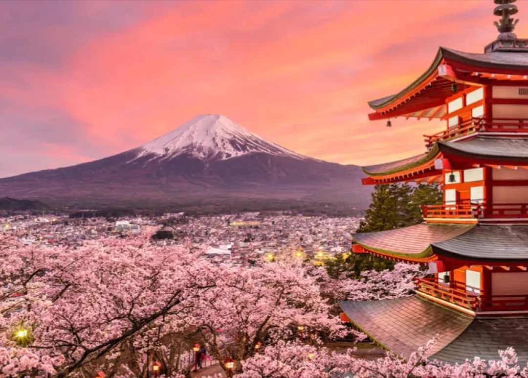 Majestic Mount Fuji crowned with snow, overlooking a serene Lake Kawaguchiko dotted with cherry blossoms.