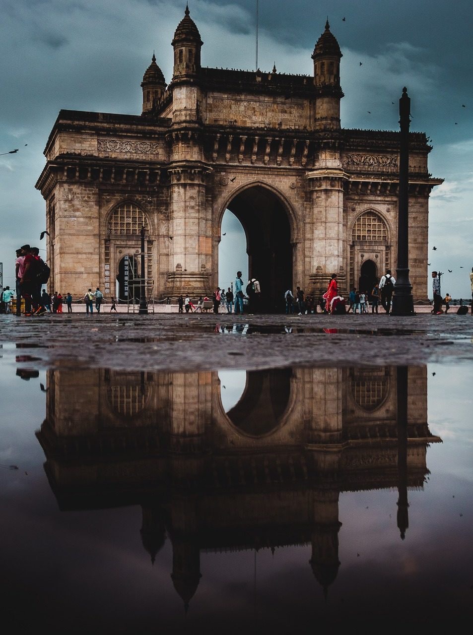 The majestic Gateway of India at sunrise, overlooking fishing boats in the Arabian Sea, bustling with early morning activity.