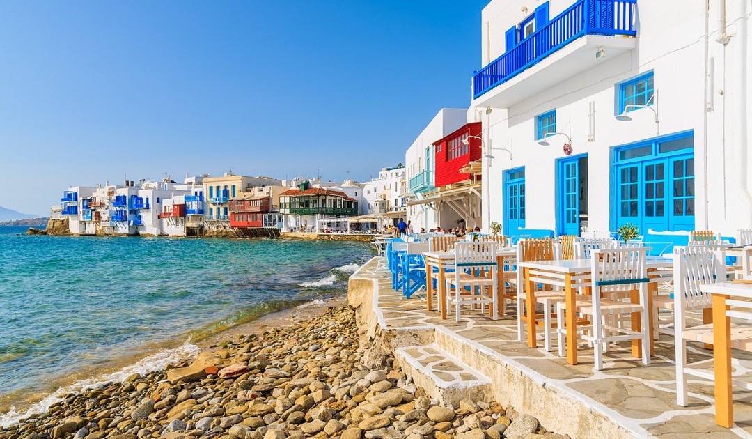 Iconic Mykonos windmills stand proudly above Little Venice's vibrant waterfront houses at sunset.