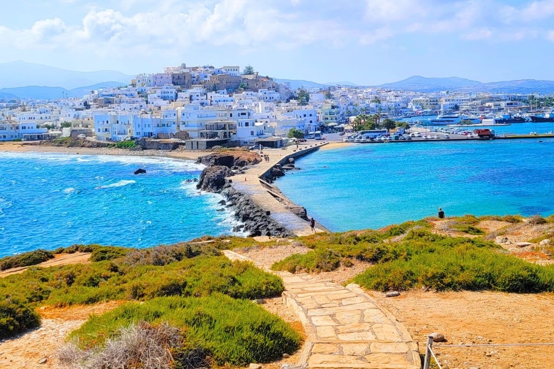 Iconic Portara, the marble gate to the ancient Temple of Apollo, standing majestically against a vibrant orange sunset over the Aegean Sea in Naxos.