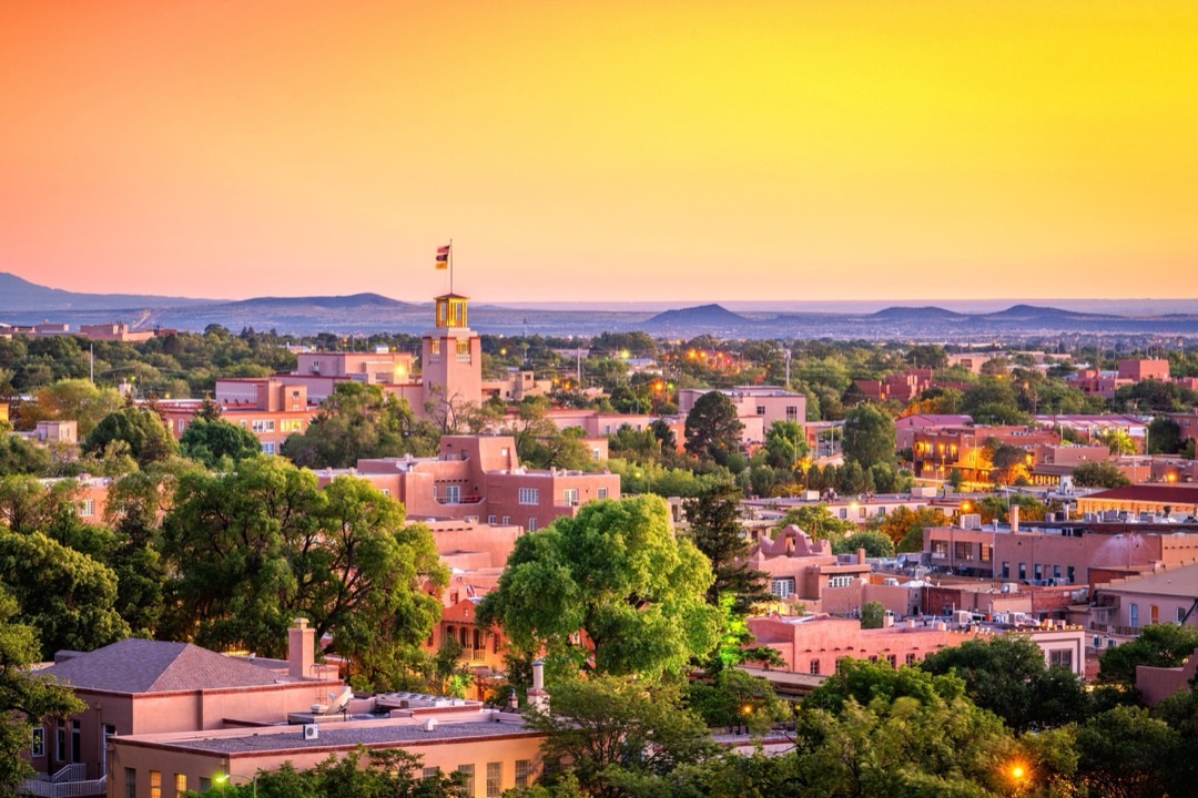 Historic adobe buildings of Santa Fe Plaza glow under the golden hour sun, bustling with activity.