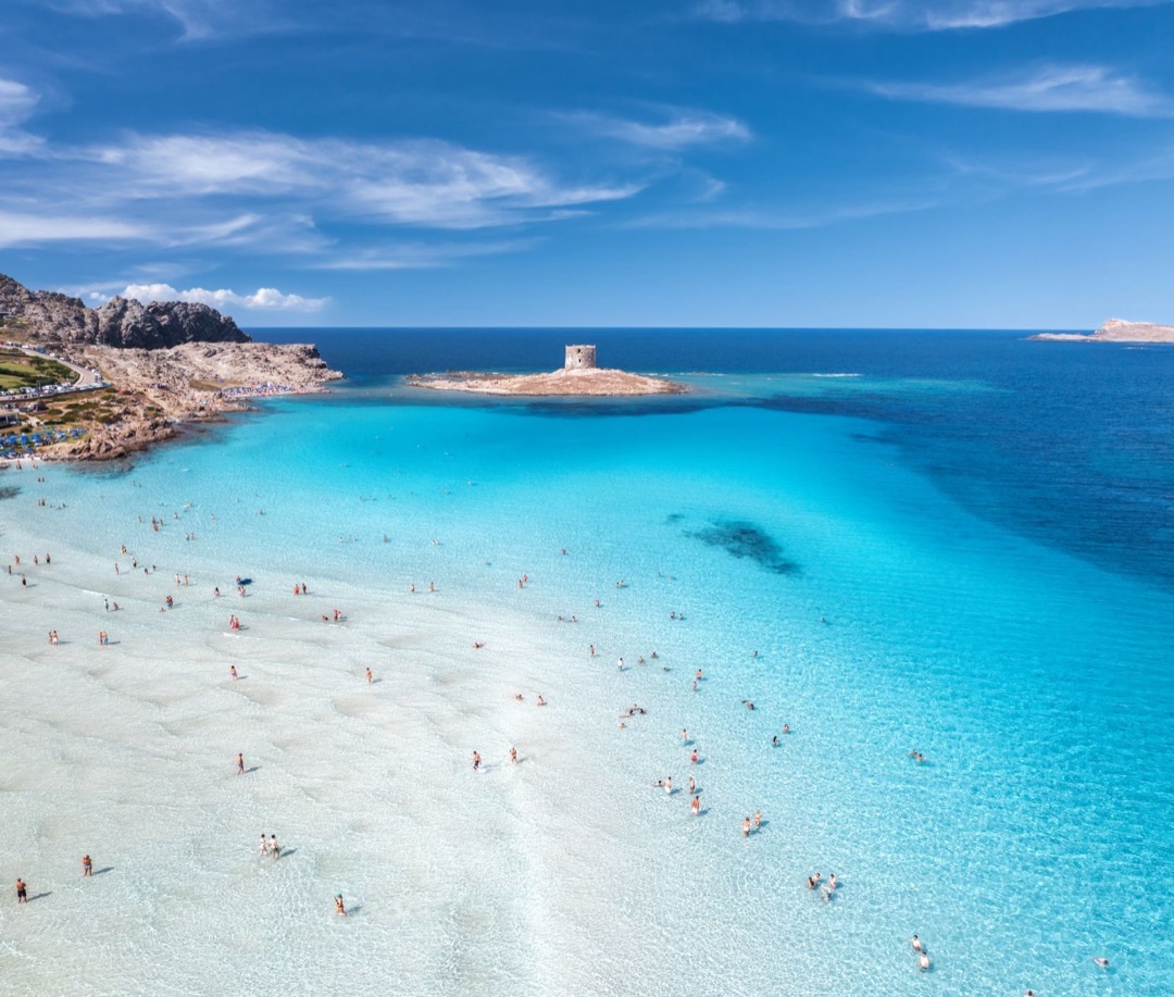 White sands of La Pelosa beach stretching into turquoise waters, with ancient watchtowers in the distance.
