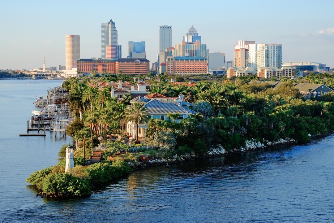 A vibrant sunset casts warm hues over Tampa's Riverwalk, with boats gently rocking on the Hillsborough River.