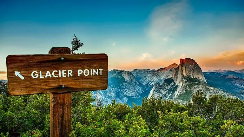 Majestic Half Dome granite monolith reflecting in the Merced River under a clear blue sky, surrounded by towering pines in Yosemite Valley.