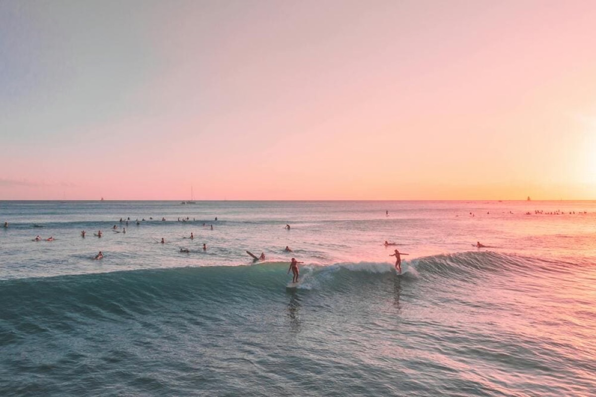 Surfers riding waves at Canggu Beach under a pink pastel sunset sky, Bali