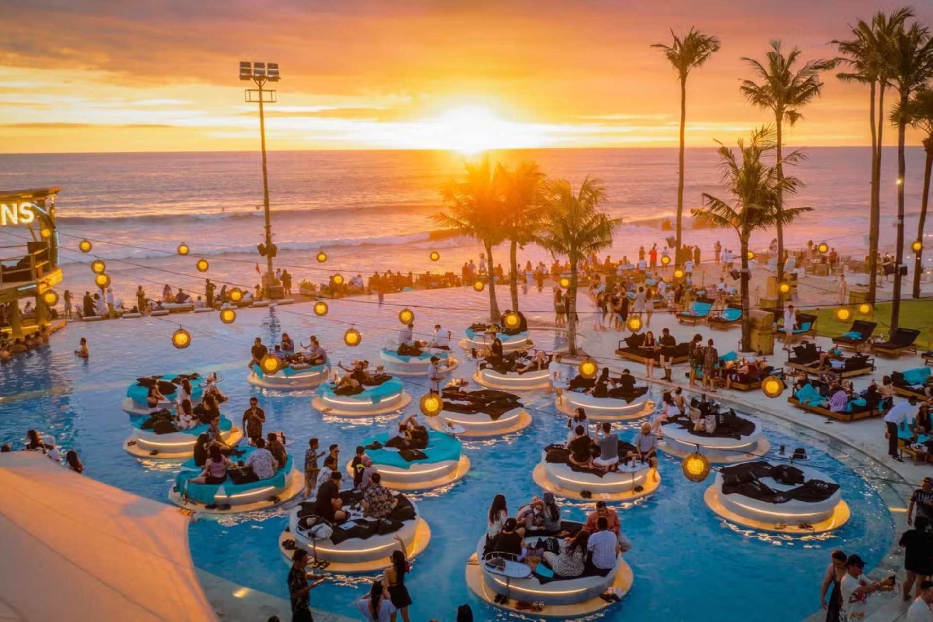 Finns Beach Club Canggu with floating lounge pods, lanterns, and golden sunset over the ocean, Bali