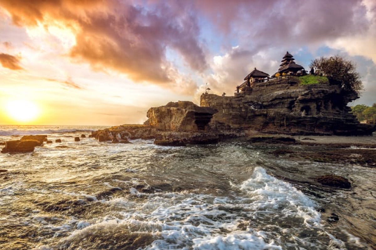Tanah Lot sea temple on rocky island with crashing waves and dramatic sunset sky, Bali