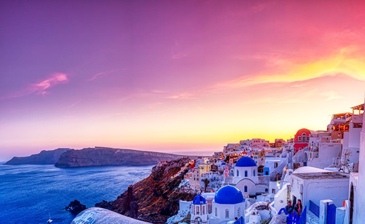 Oia village Santorini dramatic purple and golden sunset with blue dome churches