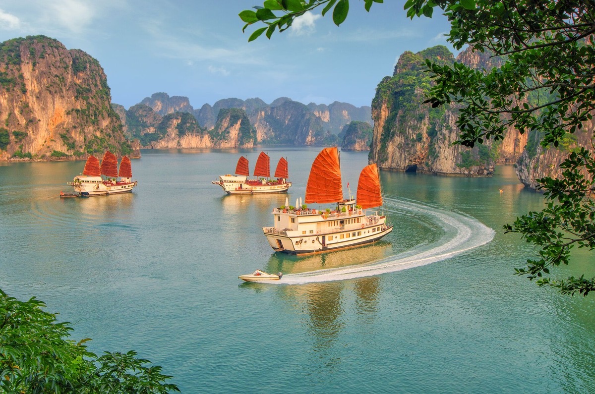 Traditional junk boat sailing through Ha Long Bay limestone karsts at golden hour