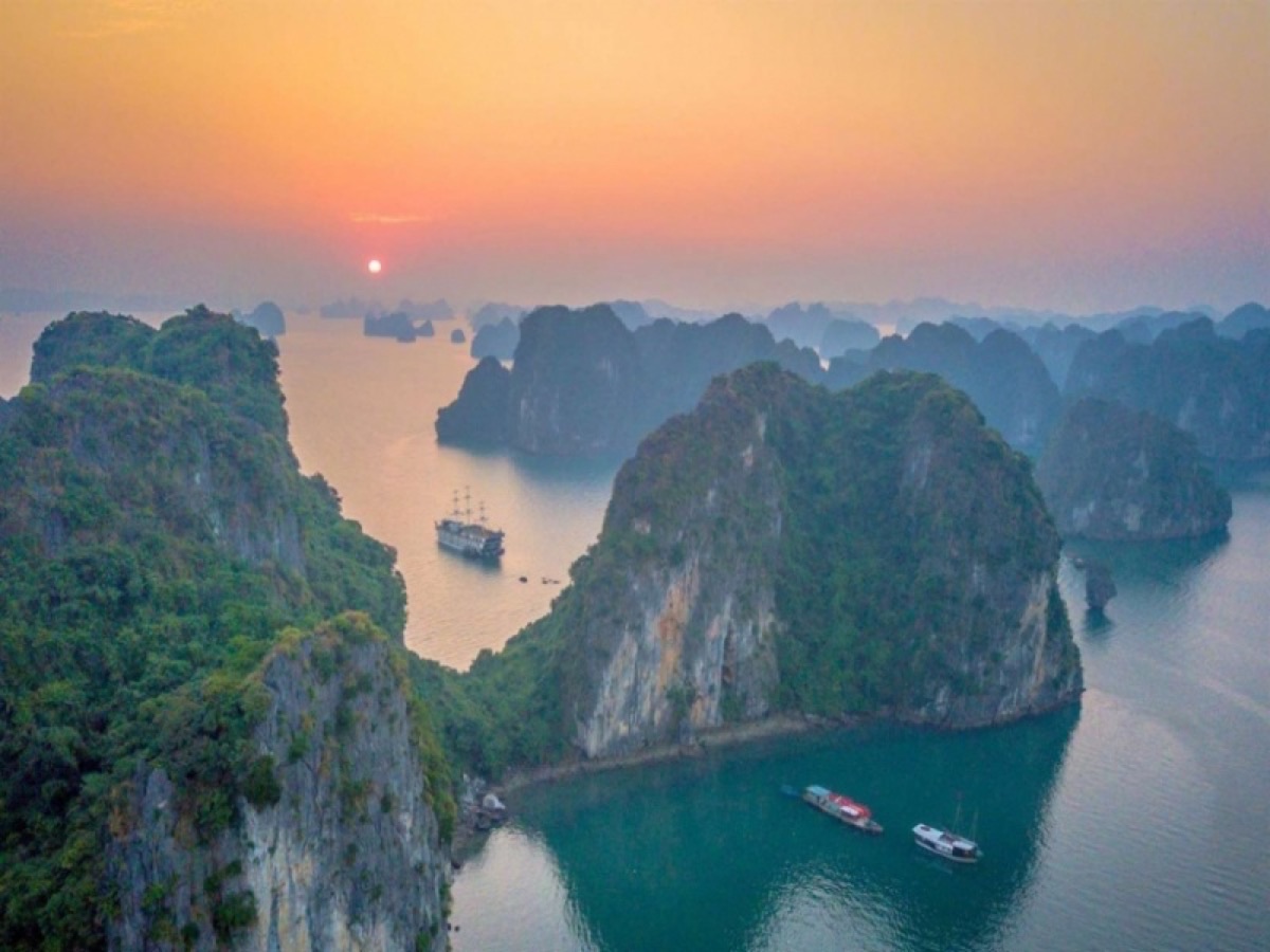 Ha Long Bay sunrise with morning mist layering between limestone karsts and cruise boats