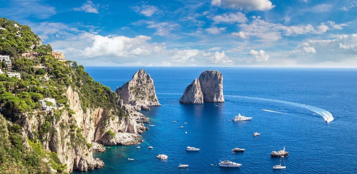 Faraglioni rock formations rising from the sea at Capri island Italy with sailboats below