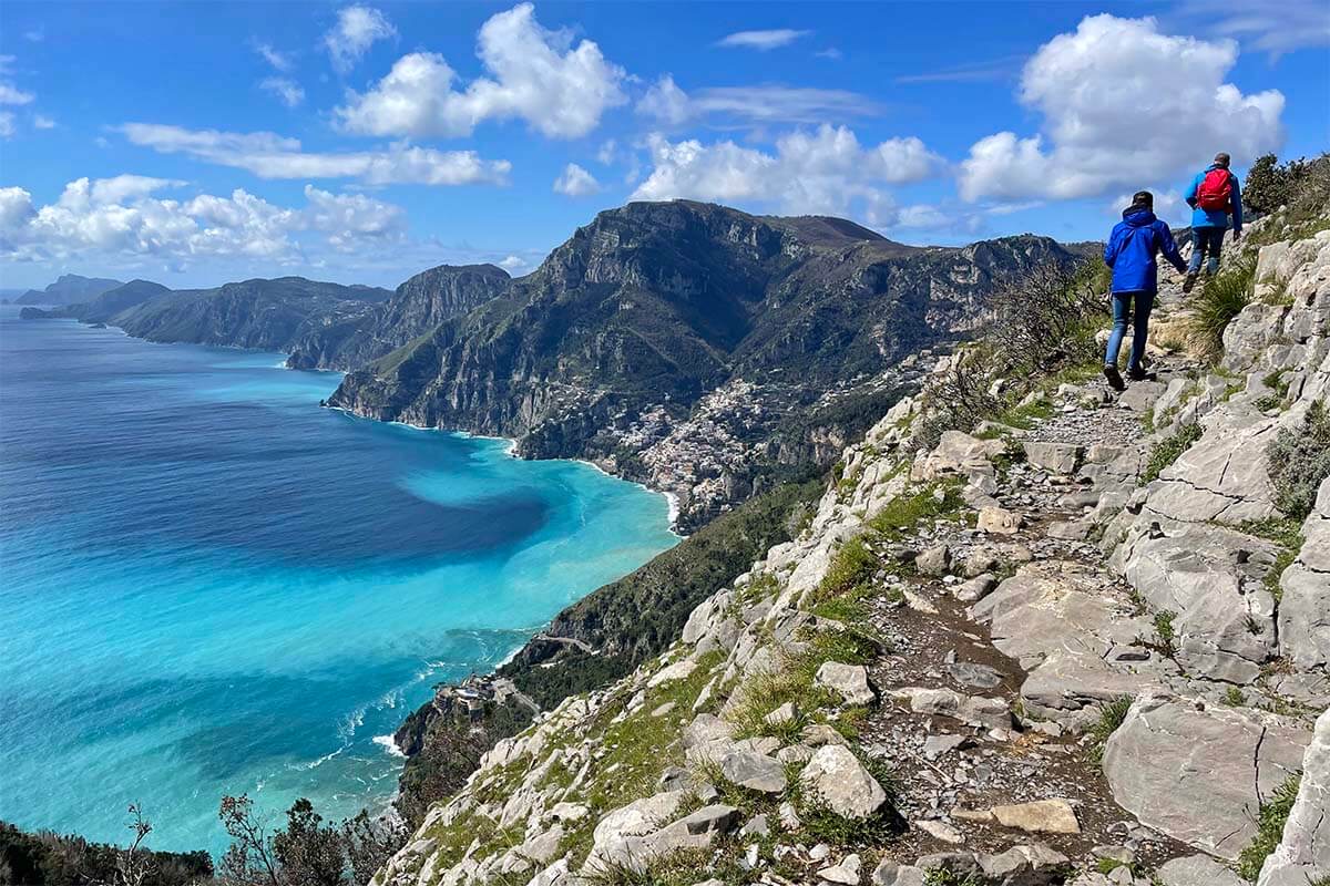 Hikers on the Path of the Gods trail with turquoise Amalfi Coast sea and dramatic cliffs below