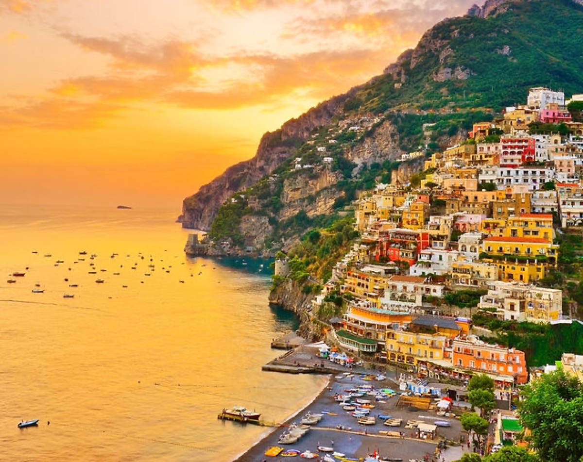 Golden hour sunset over Amalfi Coast village with colorful houses cascading to the turquoise sea