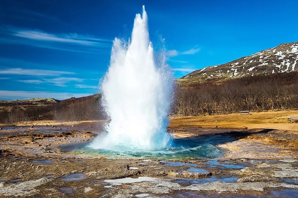 Strokkur geyser erupting with turquoise pool and snow-capped hills, Iceland
