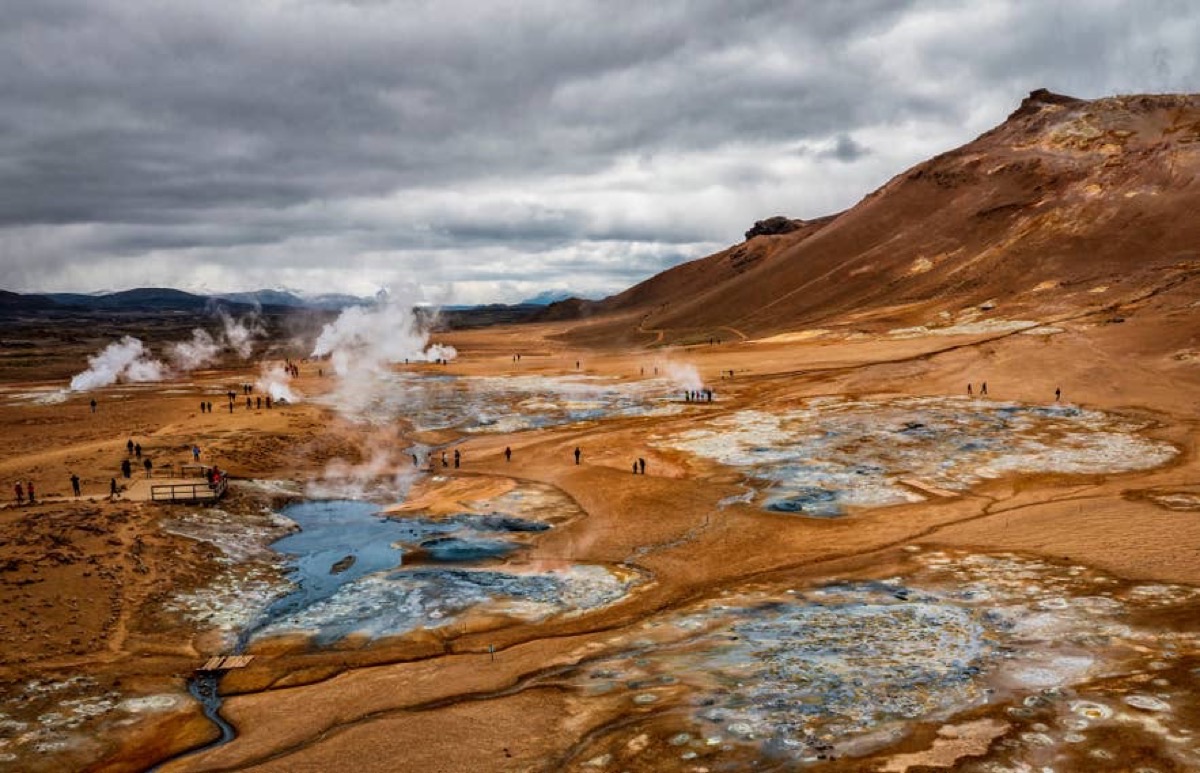 Hverir geothermal area near Lake Mývatn with rust-orange earth, turquoise mineral pools, and steam plumes under dramatic clouds