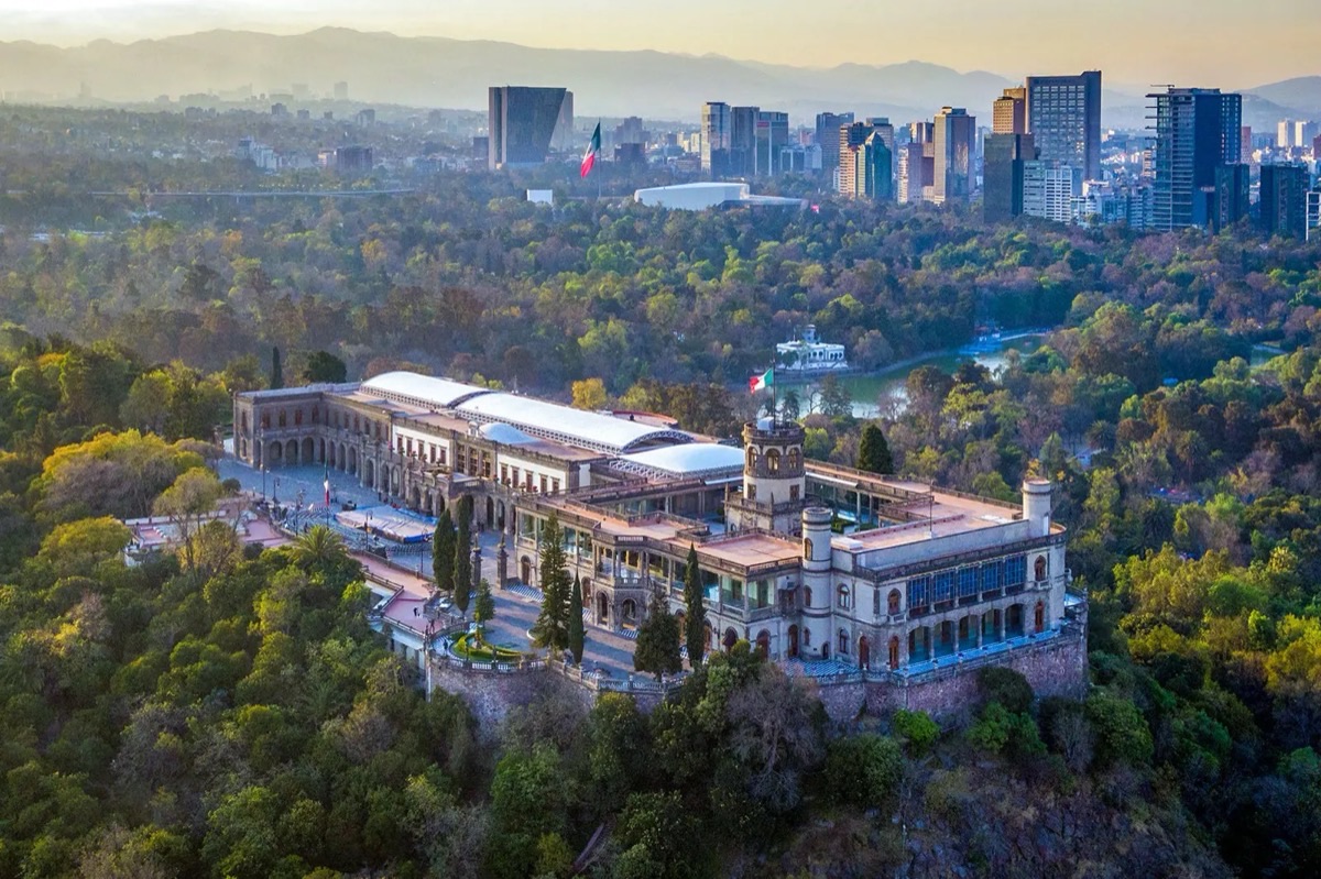 Aerial view of Chapultepec Castle at golden hour with Mexico City skyline and mountains in the background