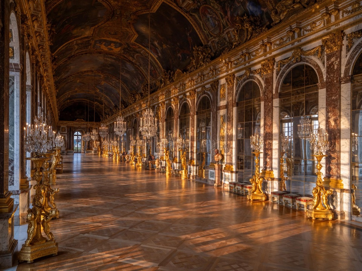Hall of Mirrors at the Palace of Versailles with ornate chandeliers and golden light streaming through the windows