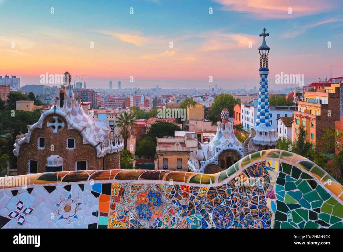 Park Güell mosaic terrace with Gaudí gingerbread towers and Barcelona skyline at sunset