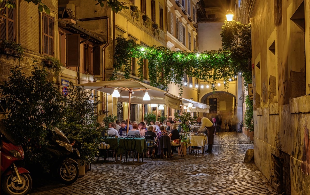 Golden evening light on Trastevere cobblestone streets with ivy-draped buildings and outdoor dining