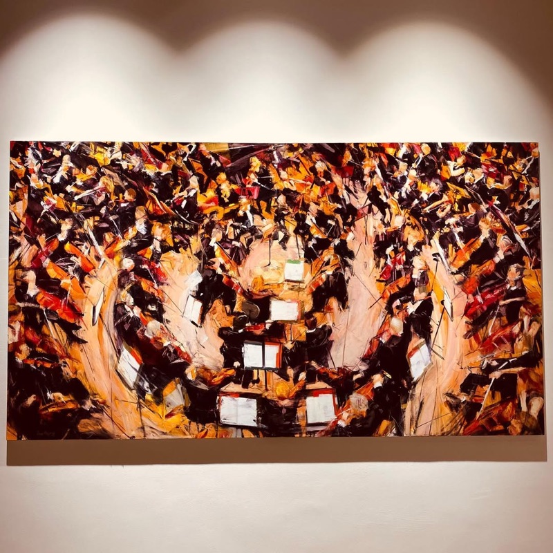 Large-scale orchestra painting on gallery wall with dramatic spotlight lighting at Fann A Porter